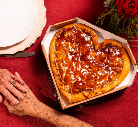 Pizza doce em formato de coração dentro da caixa, sobre toalha vermelha